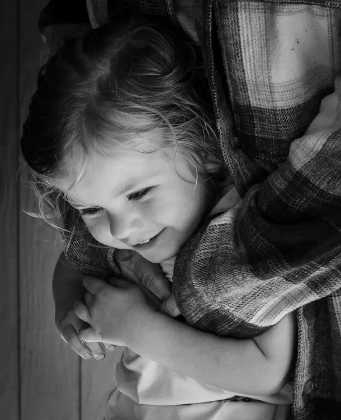 Una niña sonriente envuelta en los brazos de su madre