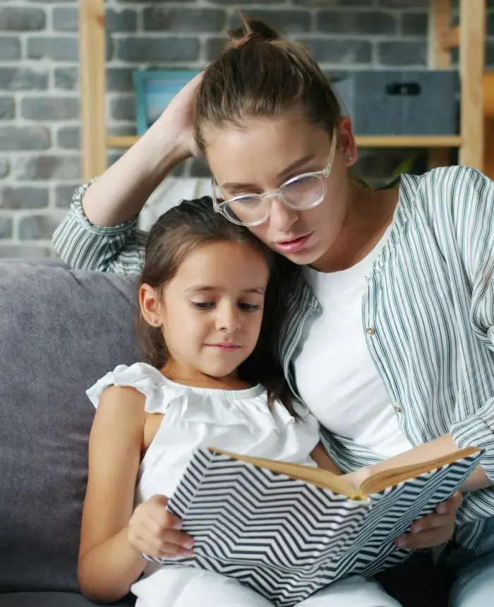 A mother and daughter reading a book together on the couch at home