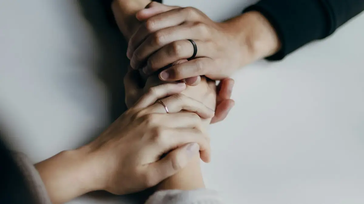 Two people holding hands across a table in a supportive conversation